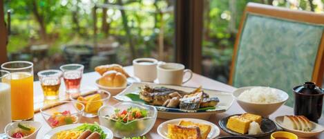 A dining table with various dishes and drinks, set in a room with a view of greenery outside.