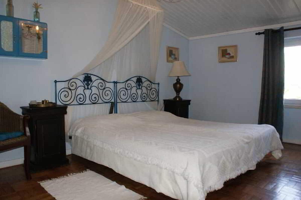 A bedroom with a bed, a nightstand, a lamp, a chair, and a window with curtains.