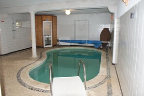 Une piscine intérieure dotée d’un plongeoir, de murs carrelés et d’une porte en bois.