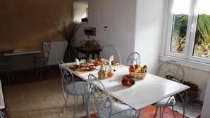 Un comedor con mesa blanca, sillas metálicas y ventana con plantas afuera.