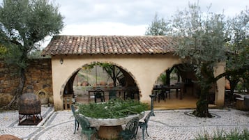 A courtyard with a tiled-roof building, stone walls, outdoor seating, and a central planter.