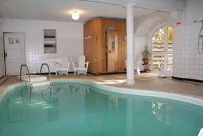Une piscine avec un sauna en bois, des murs recouverts de carreaux blancs et une porte portant l’inscription « BAUHAUS ».