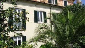 Un edificio de dos pisos con techo plano, contraventanas verdes y una chimenea.