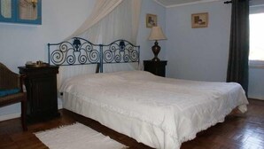 Un dormitorio con cama, mesita de noche, lámpara, silla y ventana con cortinas.