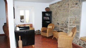 Una sala de estar con una pared de piedra, un sofá de cuero negro, sillas de mimbre, una estantería y una guitarra.