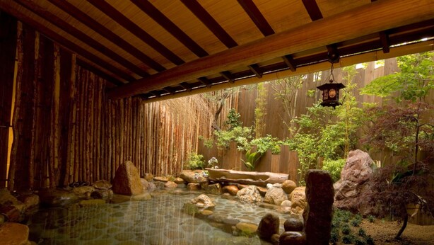 Ein traditionelles japanisches Onsen mit einem Steinhotspring, Holzbalken und einem Bambuszaun.