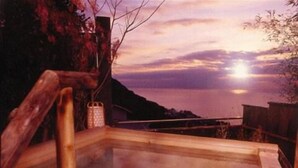 Ein Thermalbad mit Holzgeländern und Blick auf das Meer bei Sonnenuntergang.