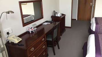 Ett hotellrum med en byrå i trä, ett skrivbord, en spegel, en säng med ett lila och vitt sängöverkast och en dörr med en träram.