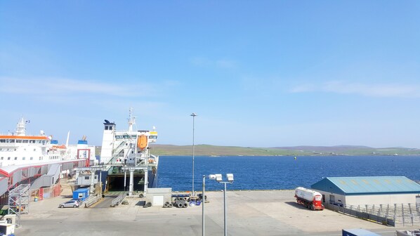A ferry dock with a large ferry, a small truck, and a building with a blue roof.