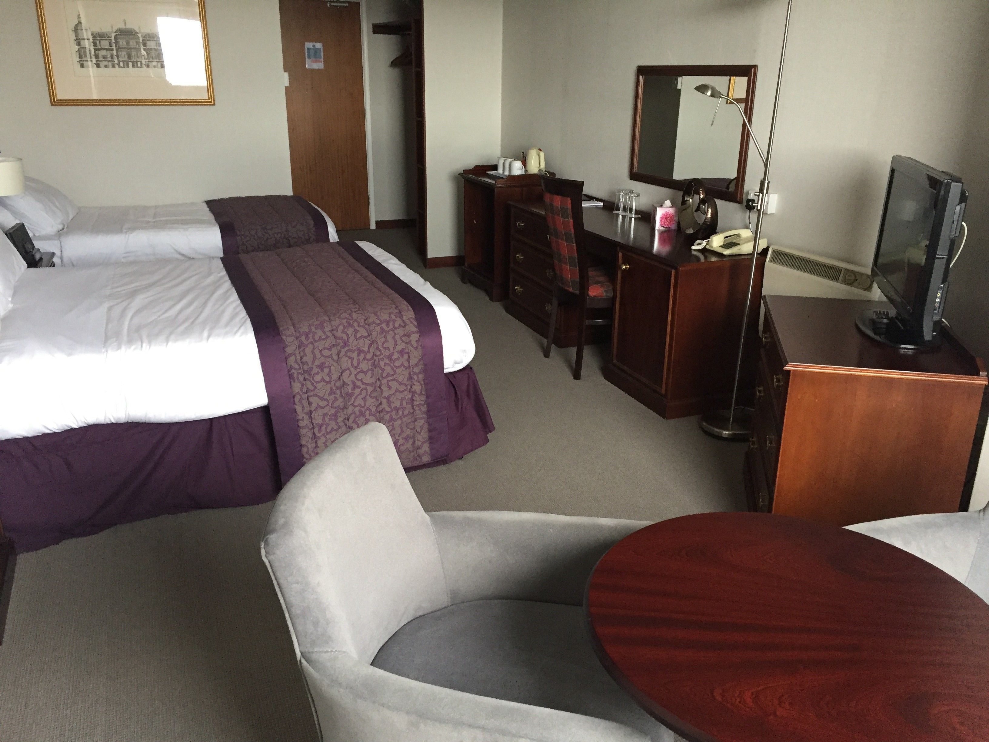 A hotel room with two beds, a desk with a computer, a chair, and a television.