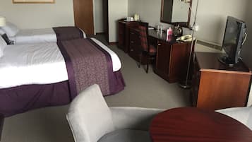 Una habitación de hotel con dos camas, un escritorio con ordenador, una silla y un televisor.