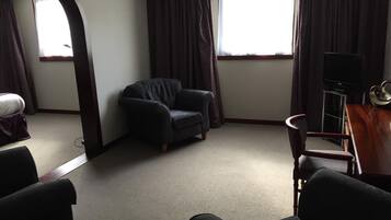 Een hotelkamer met een donker leren fauteuil, een houten bijzettafeltje met een televisie en een groot raam met gordijnen.