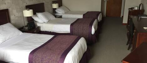 A hotel room with three beds, a desk, and a door.