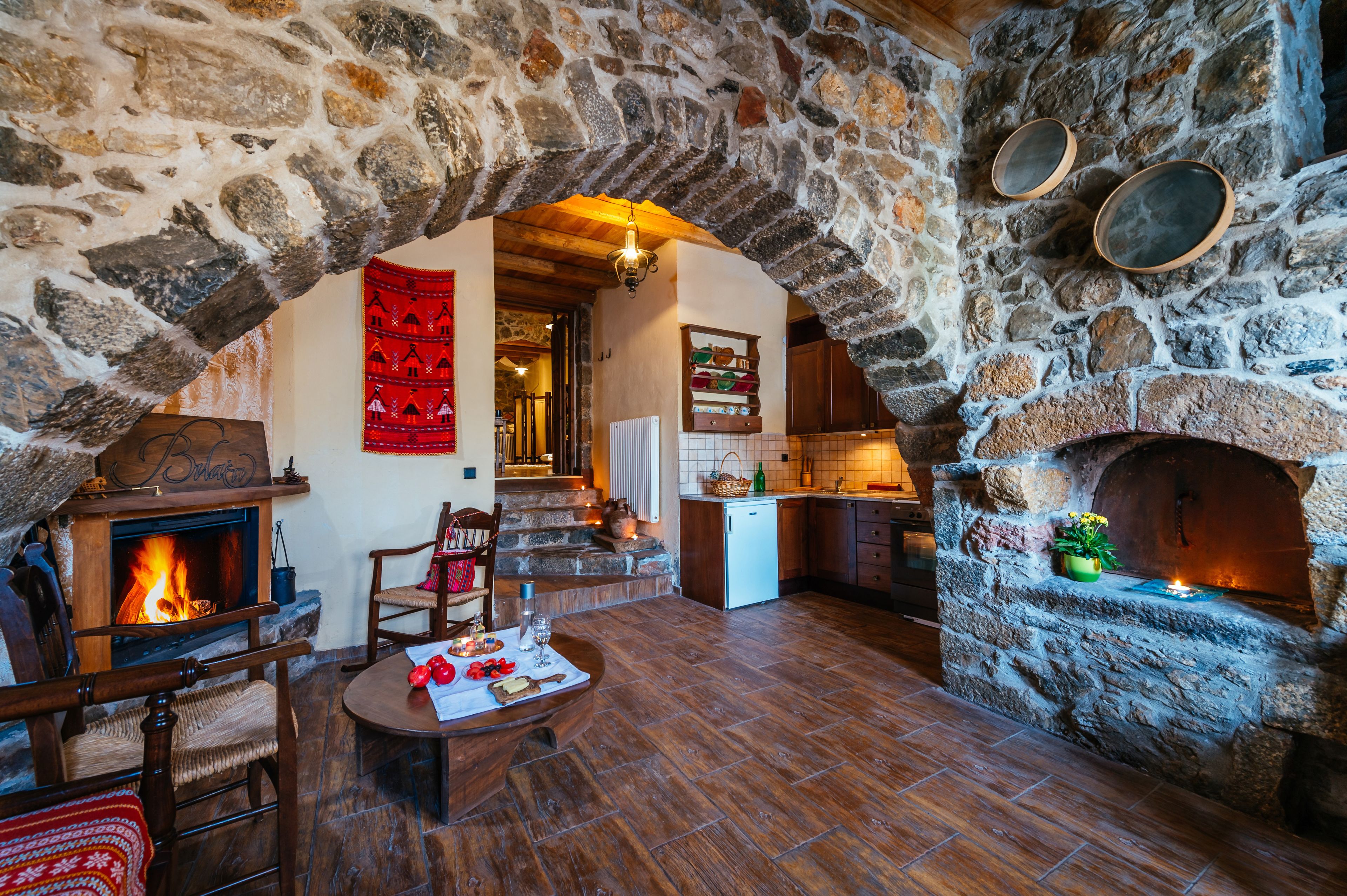 Interior con paredes de piedra, chimenea, muebles de madera y zona de cocina.