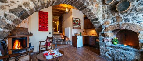 Interior com paredes de pedra, lareira, móveis de madeira e cozinha.