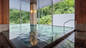 Una piscina interior moderna con paredes de vidrio transparente, suelo de madera y vistas a un exuberante follaje exterior.