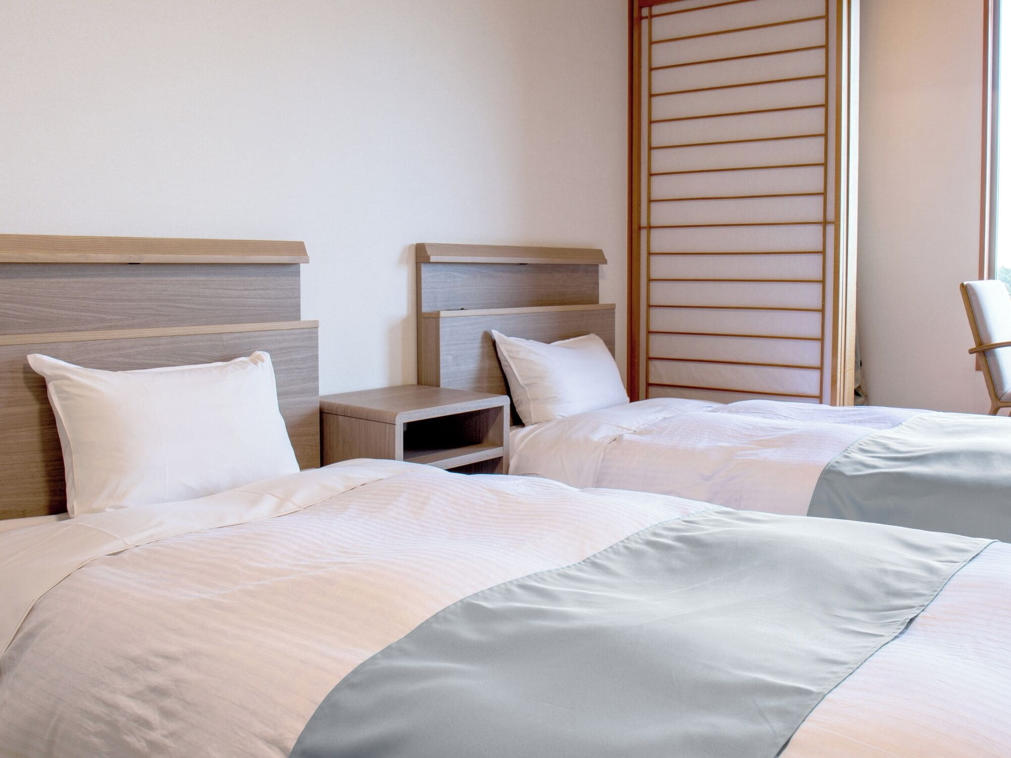 A hotel room with two beds, wooden headboards, a nightstand, and a window with blinds.