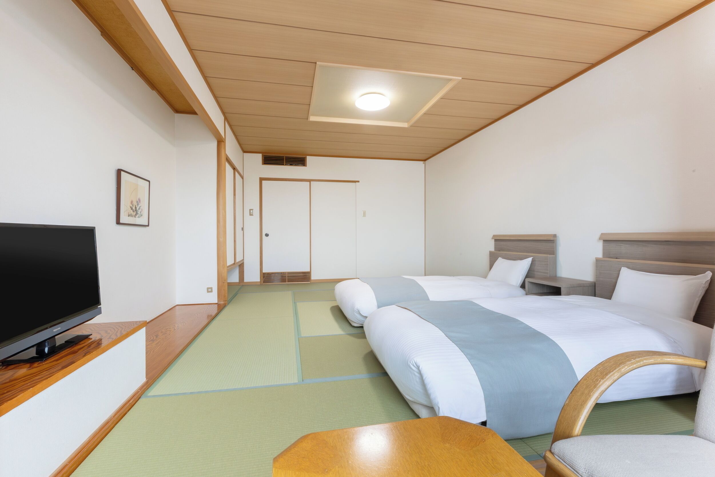 A hotel room with two beds, a television on a wooden stand, and a tatami mat floor.