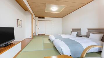 A hotel room with two beds, a television on a wooden stand, and a tatami mat floor.