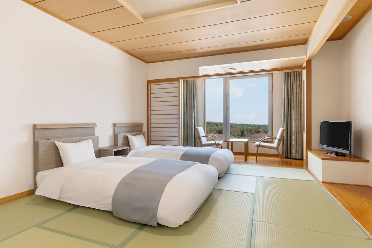 Ett hotellrum med två sängar, en TV, en stol och utsikt över omgivningarna.