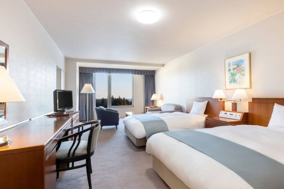 Ett hotellrum med två sängar, ett skrivbord med en tv, en stol och utsikt över omgivningarna.