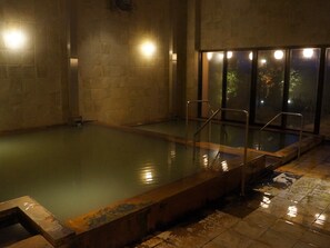 A dimly lit indoor swimming pool with tiled walls and a metal pool ladder. - Hotel Kadoman (Aso)
