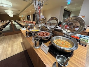 A buffet area with various food options, including sausages, a soup pot, and a hot pot station. - Hotel Kadoman (Aso)