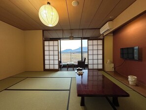 A traditional Japanese room with tatami flooring, a low table, a chair, and a sliding door with a view of mountains. - Hotel Kadoman (Aso)