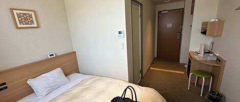 A hotel room with a bed, a desk, a chair, and a trash bin.