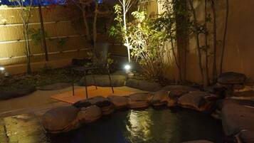 Un espacio al aire libre de noche con un pequeño estanque, rocas y una silla.
