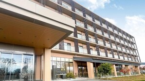 Ένα πολυώροφο ξενοδοχείο με μοντέρνο σχεδιασμό, το οποίο διαθέτει μια εντυπωσιακή είσοδο με γυάλινες πόρτες και ένα στεγασμένο πεζοδρόμιο.