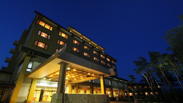 A multi-story hotel with a covered entrance, large windows, and a stone wall in front. - Yahatakan (Sado)