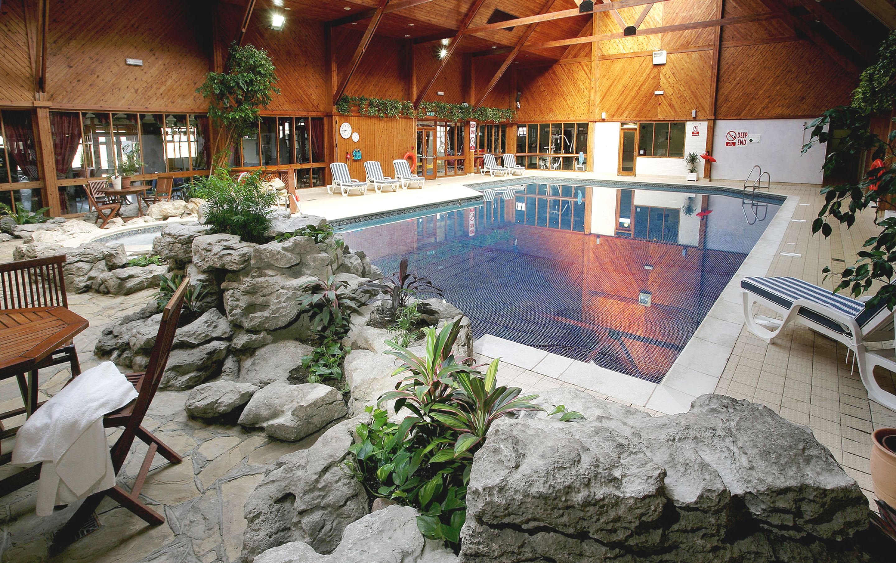 Una piscina interior con paisaje rocoso, sillas de descanso y arquitectura de madera.
