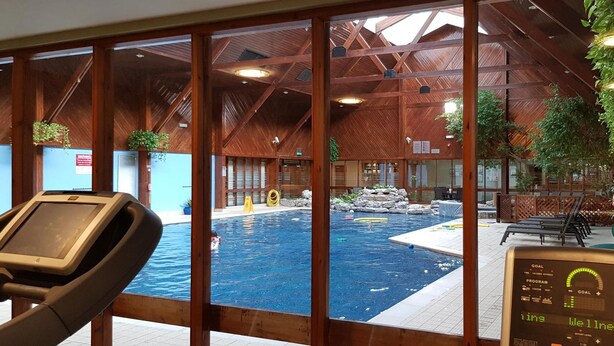 Une piscine intérieure avec des poutres en bois et une vue sur l’espace piscine grâce à de grandes fenêtres.