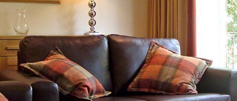 A dark brown leather sofa with plaid pillows, a standing lamp, and a glass coffee table.