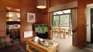 L’intérieur d’un chalet en bois comprend un lit, un téléviseur, un coin repas et une table avec une théière et un magazine.