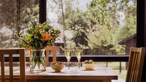 Une table en bois sur laquelle se trouvent un vase de fleurs, deux verres de vin blanc et deux bols remplis de noix et d’olives.
