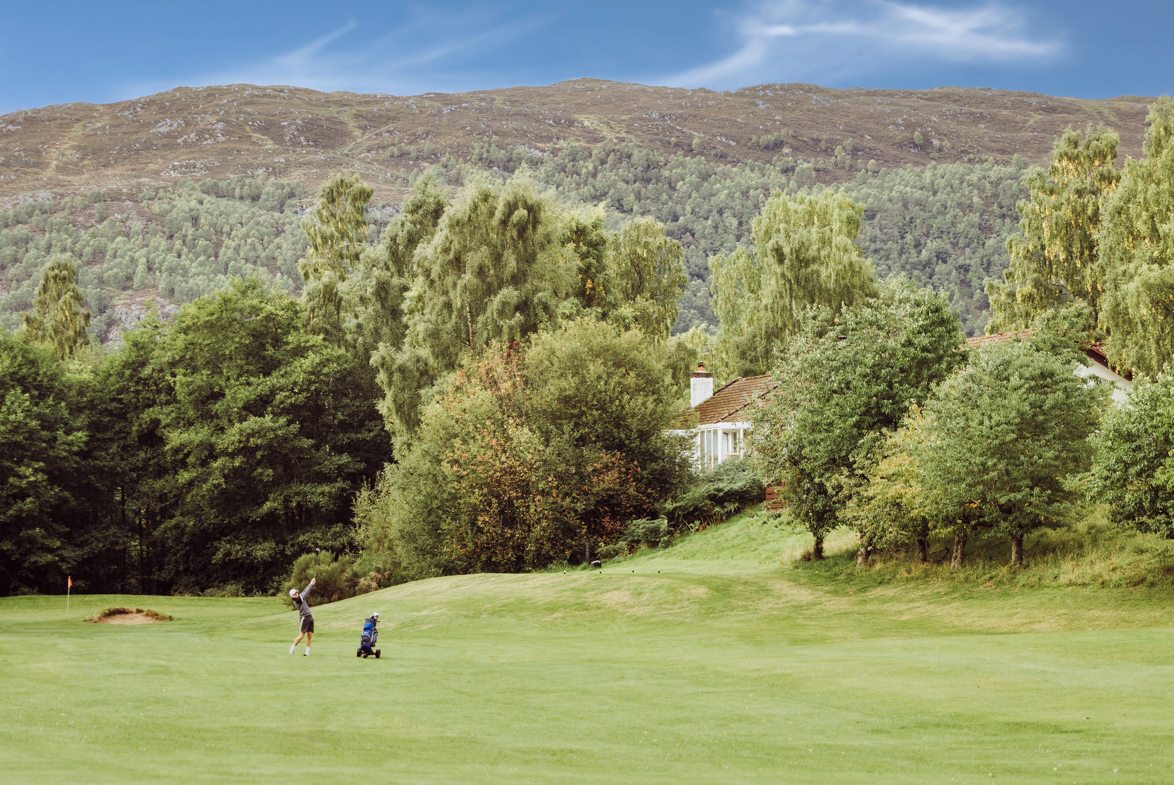 Ein Golfplatz mit einem Haus im Hintergrund, umgeben von Bäumen und Hügeln.