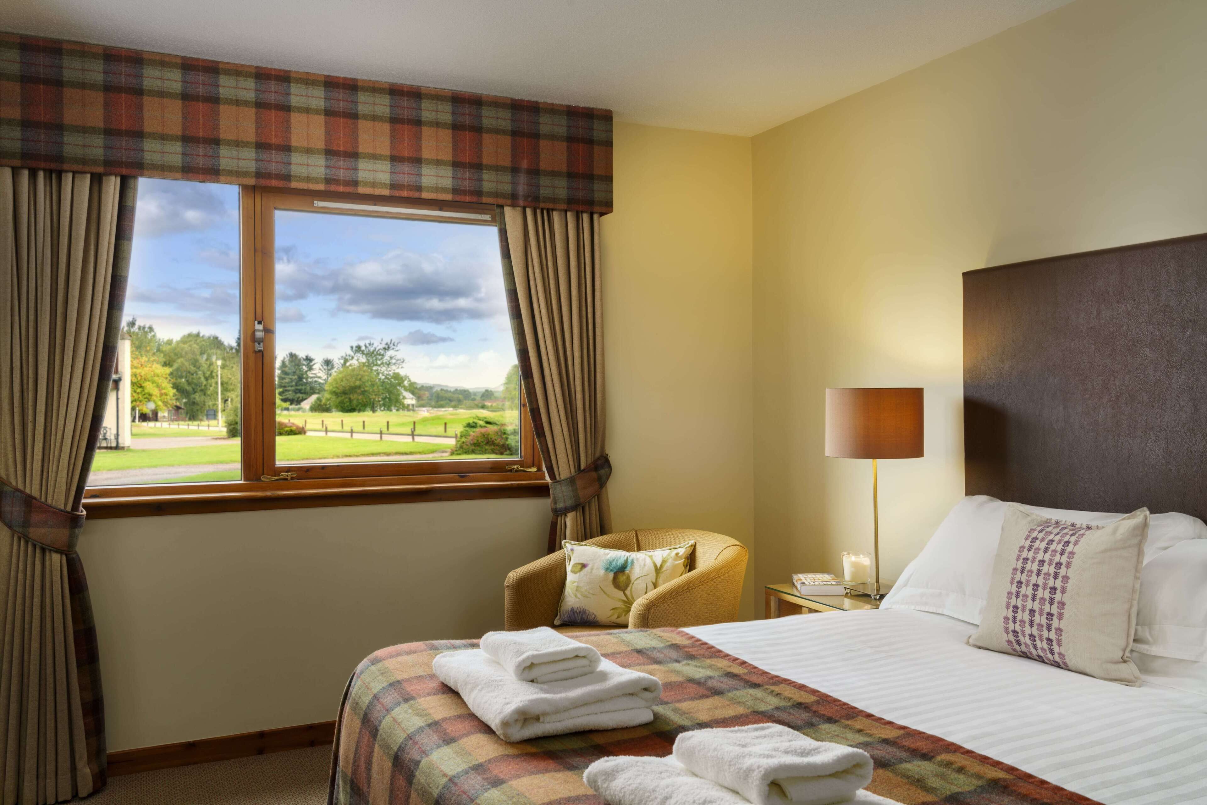 A hotel room with a bed, a chair, a lamp, and a view of a green landscape through the window.