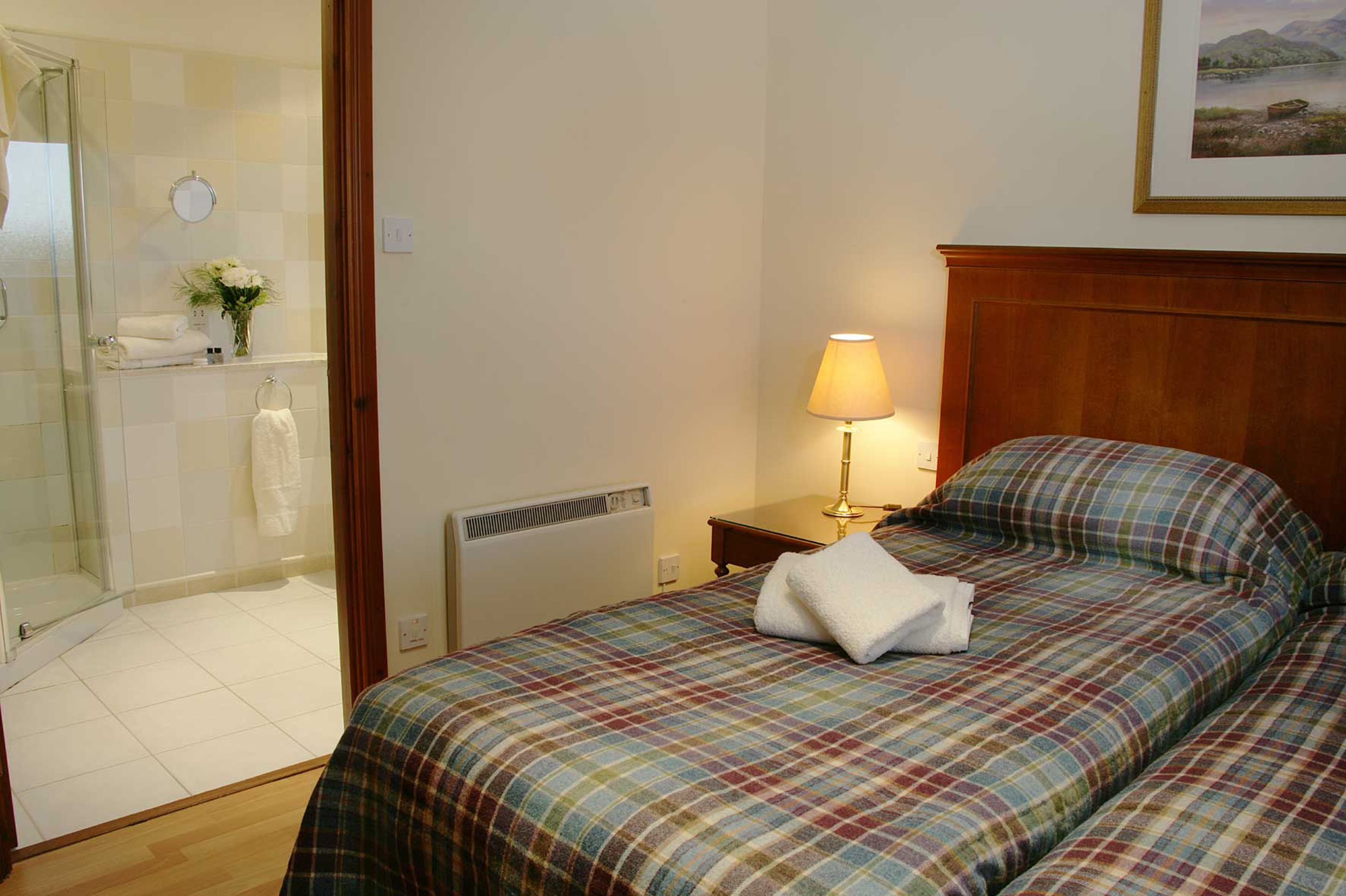 Una habitación de hotel con cama, mesita de noche, lámpara, ducha y vistas al exterior.