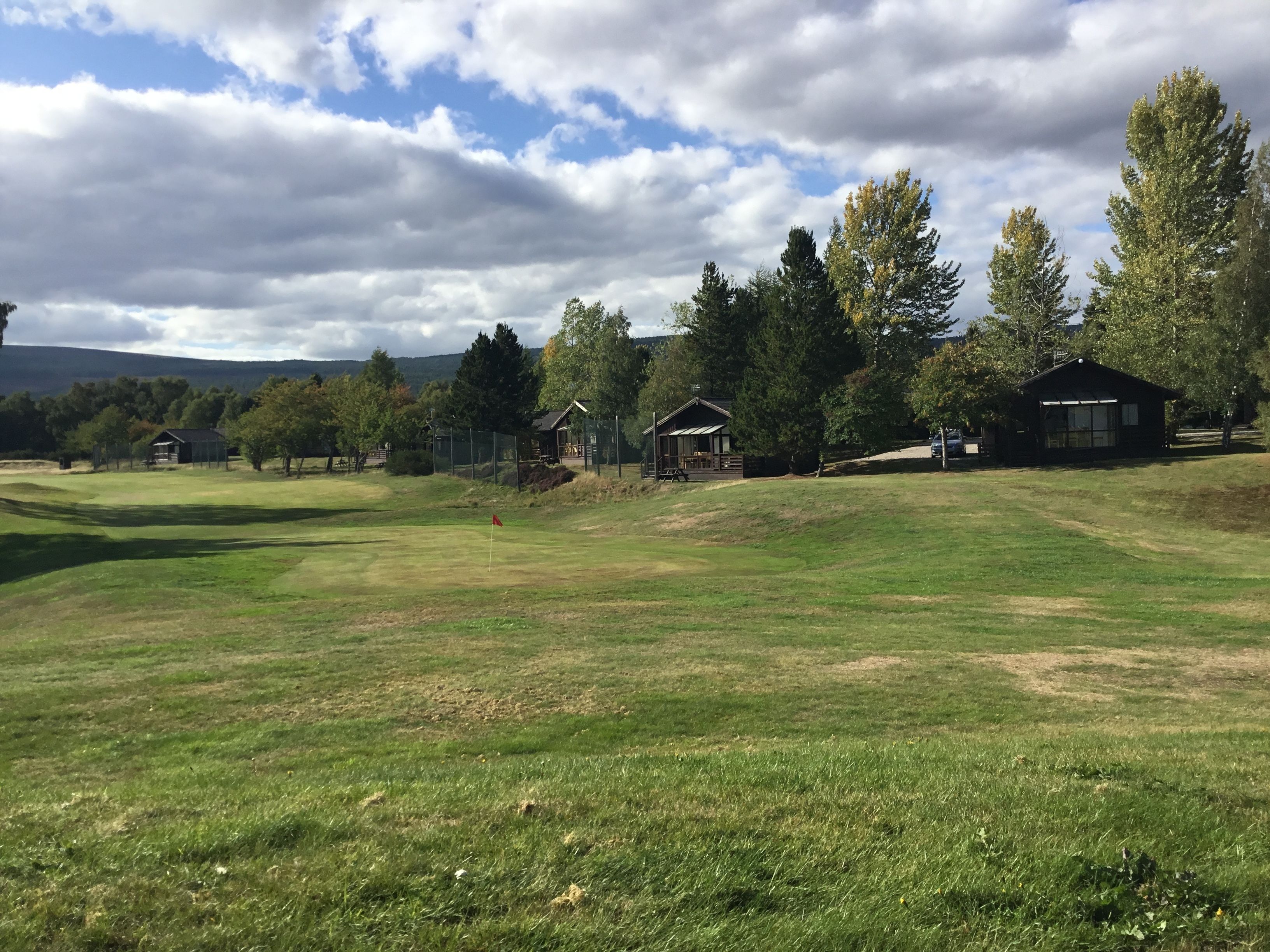 Un parcours de golf avec des bunkers, un drapeau et plusieurs cabanes en bois.