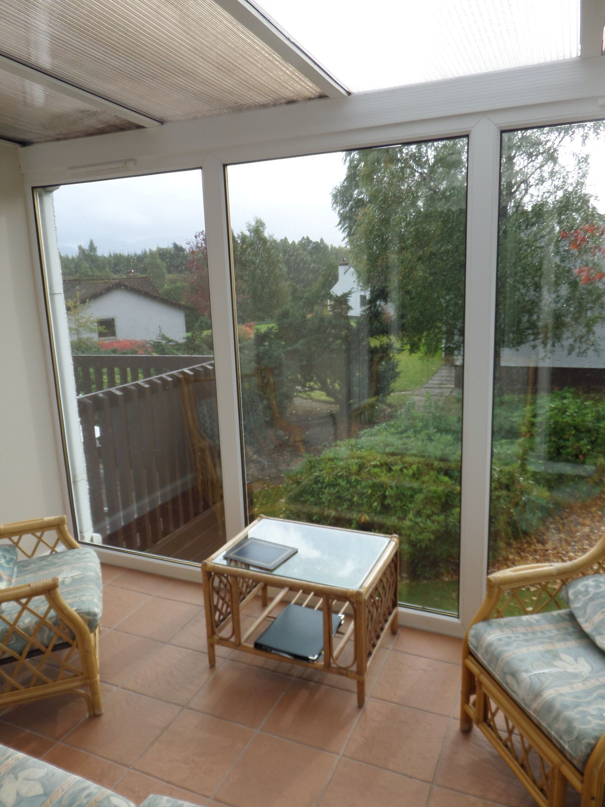Un solárium con grandes puertas de cristal, mobiliario de mimbre y suelo de baldosas.