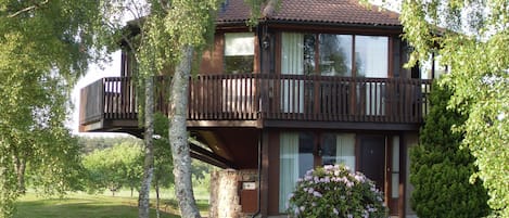A two-story house with a balcony, surrounded by trees and a well-maintained lawn.