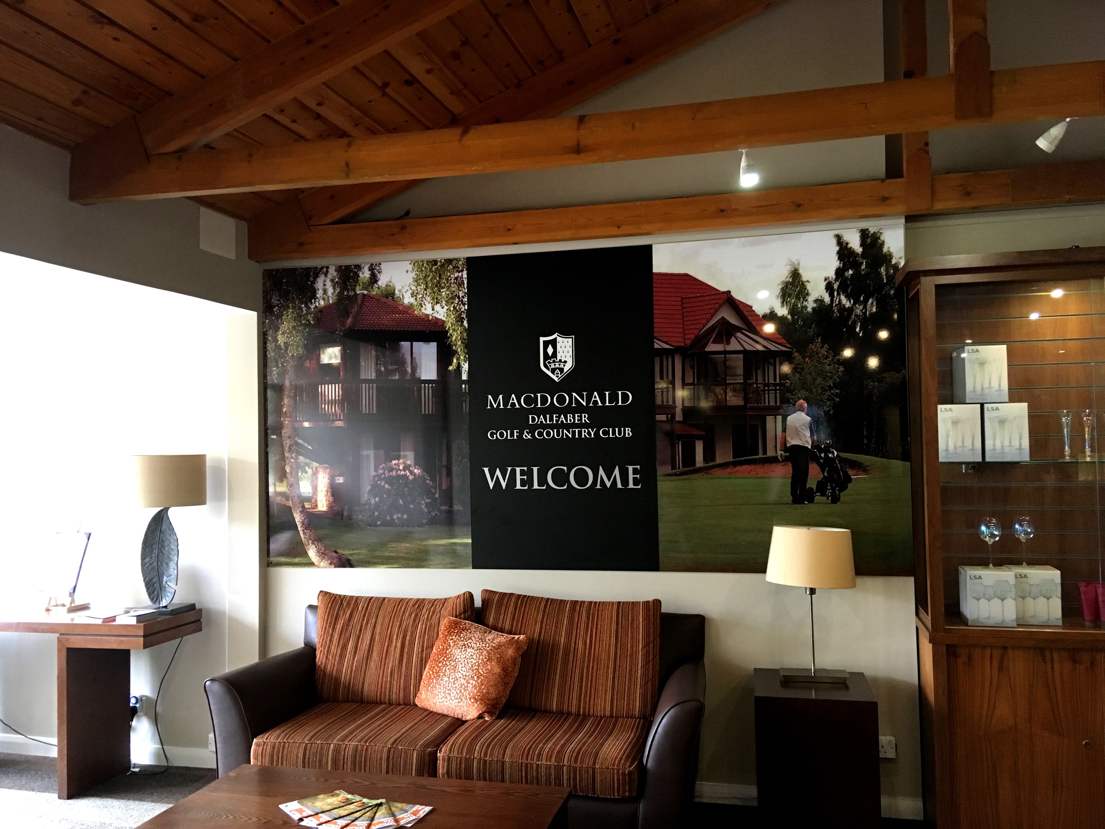Un cuarto acogedor con techo de madera, un sofá, una mesita de café y una pared con el logo de un club de golf y un letrero de bienvenida.