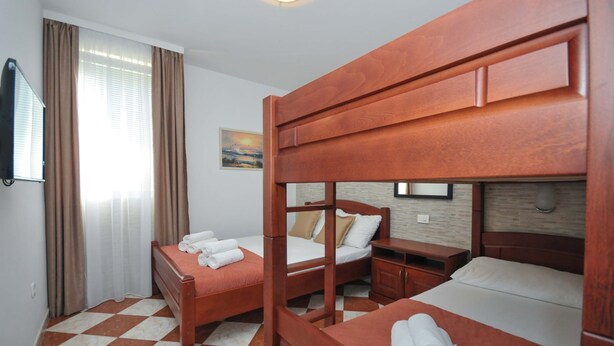 Una habitació d'hotel amb tres llits de fusta, una petita taula de nit, un televisor fixat a la paret i un paviment a escacs.