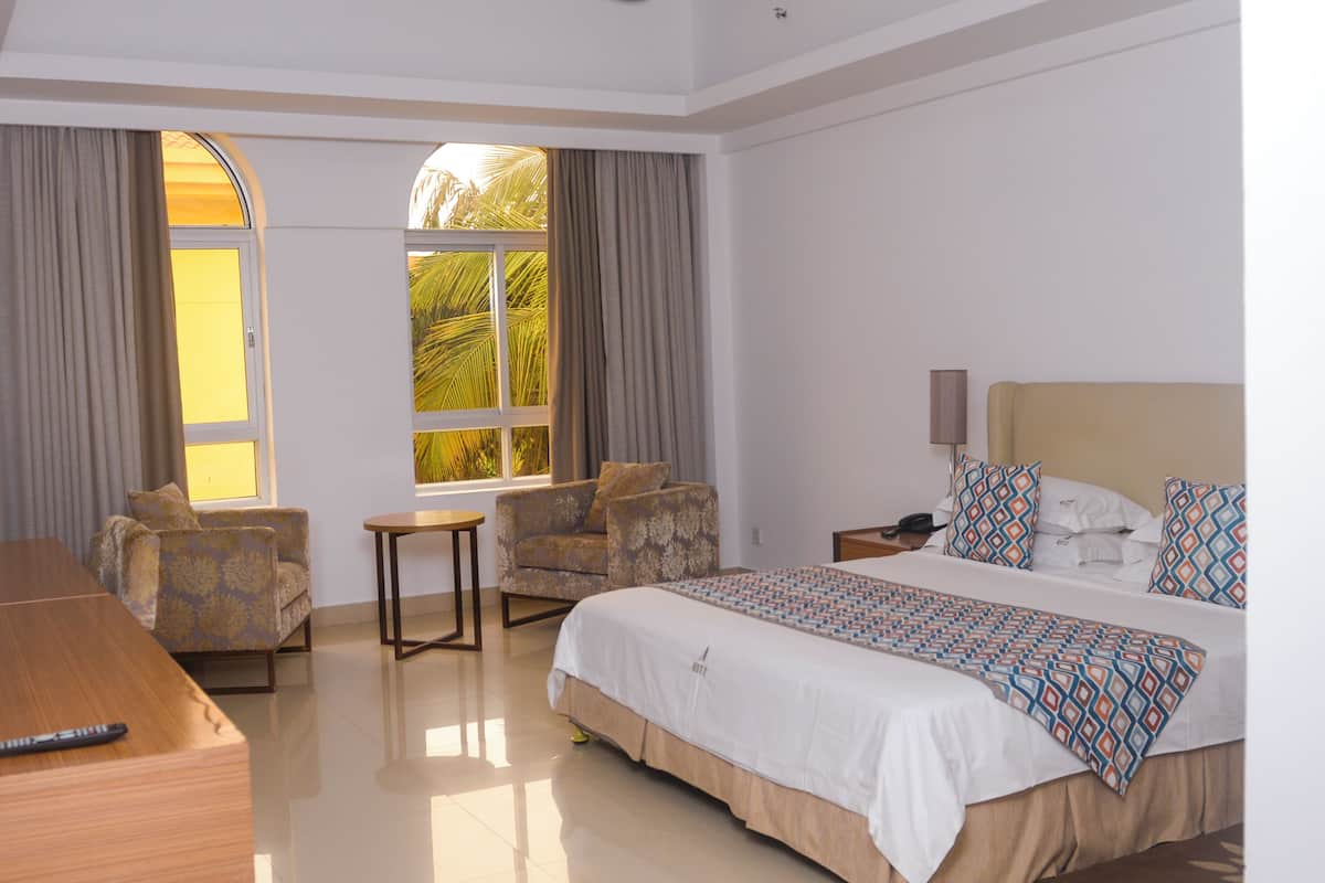 A hotel room with a large bed, two armchairs, a small table, and a nightstand.