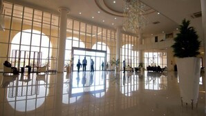 Un lobby amplio con ventanas grandes, piso pulido y una lámpara de araña central.
