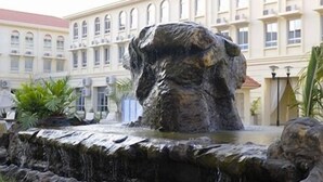 Un patio con una fuente de piedra, asientos al aire libre y un edificio con ventanas de arco.
