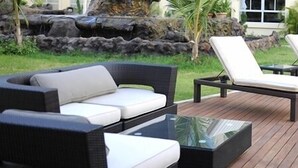 Un área junto a la piscina con sillones de descanso y un sofá, una mesa de vidrio y la piscina.