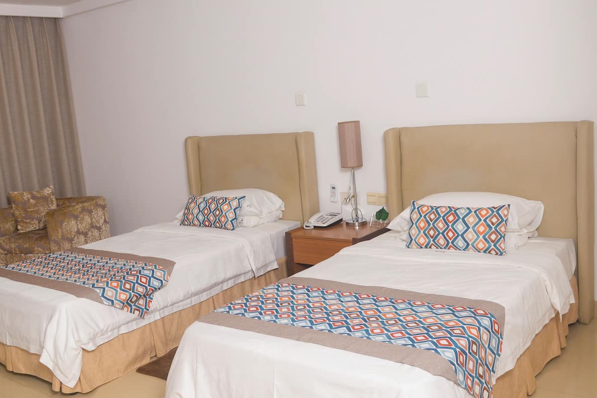 A hotel room with two beds, each with patterned bedding and a bedside table with a lamp and phone.